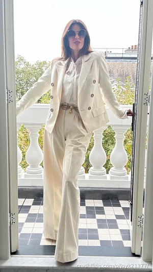 Woman in cream suit and sunglasses standing on balcony with checkered floor.