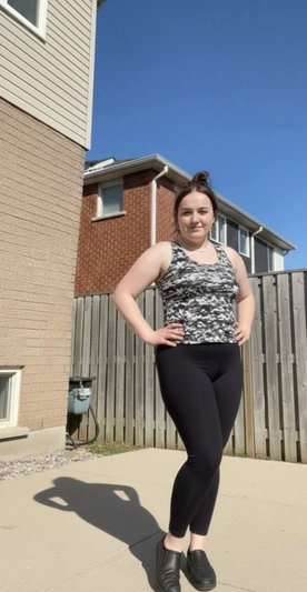 Woman in camo tank top and black leggings standing outdoors in a residential yard.