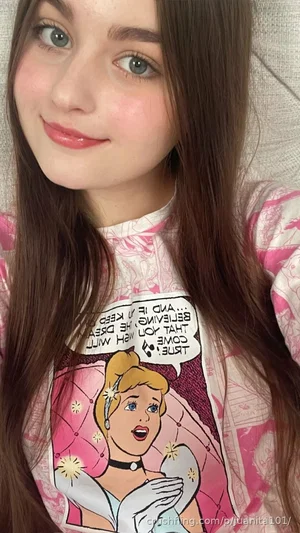 Woman with long brown hair wearing pink princess-themed shirt, indoor selfie.