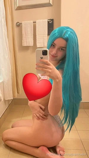 Woman with blue wig kneeling in bathroom, holding phone for mirror selfie, wearing minimal lingerie.
