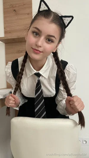 Woman with braided hair and cat ears, wearing a white shirt, tie, and black vest, indoors.