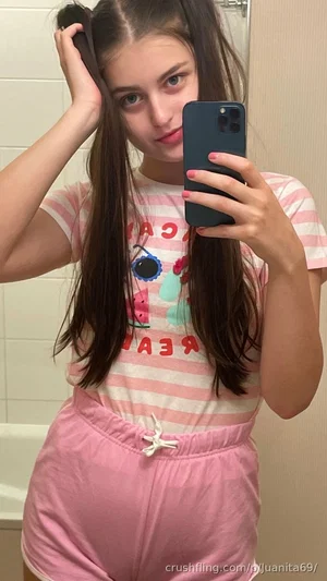 Woman with long dark hair in striped shirt and pink pants taking mirror selfie in bathroom.