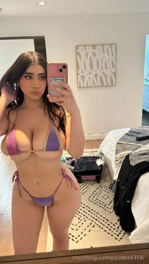 Woman in purple and pink bikini taking mirror selfie in bedroom.