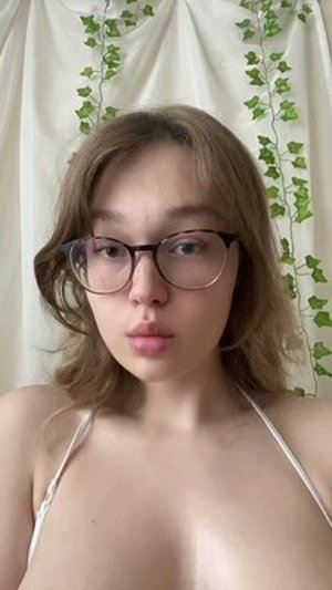 Woman with glasses in white halter top before ivy curtain.