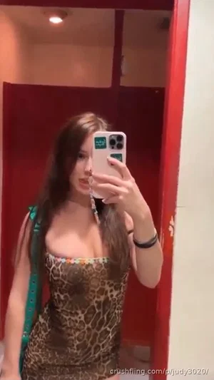 Woman in leopard print top taking mirror selfie in red room.