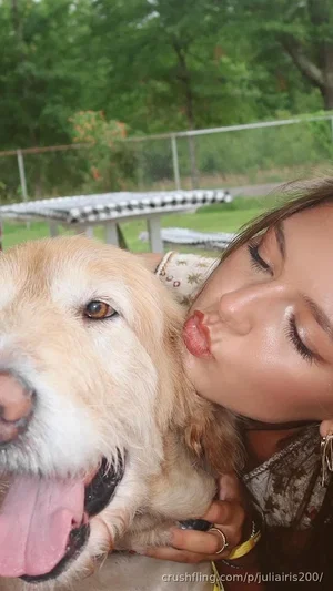 Woman with dog outdoors, wearing patterned top, kissing dog's cheek.