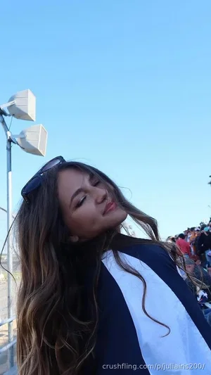 Woman with long brown hair wearing a black and white jacket, posing outdoors under a clear sky.