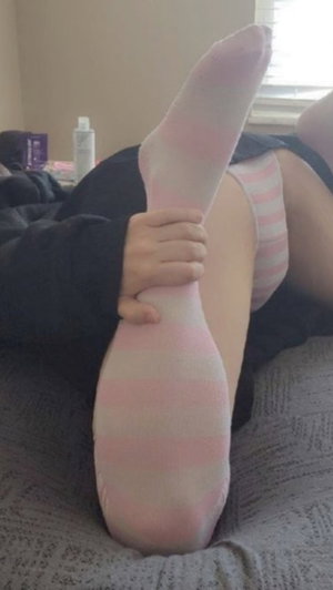 Woman in pink striped socks and black shorts lying on bed, holding foot.