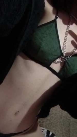 Woman in green lace bra and black robe, showing midriff and necklace, indoor setting.