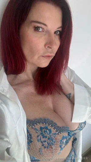Woman with red hair in blue lace lingerie and white shirt, indoor selfie.