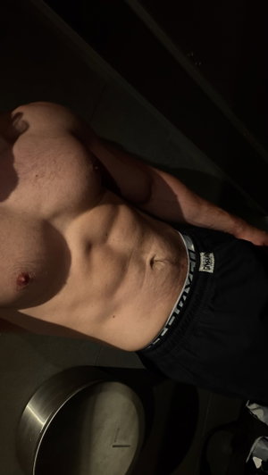 Shirtless man with defined abs wearing black shorts, standing indoors.
