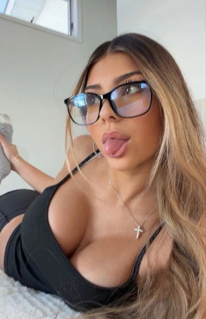 Blonde woman in black top and glasses posing indoors.