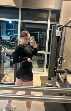 Woman in black athletic wear taking mirror selfie in gym.
