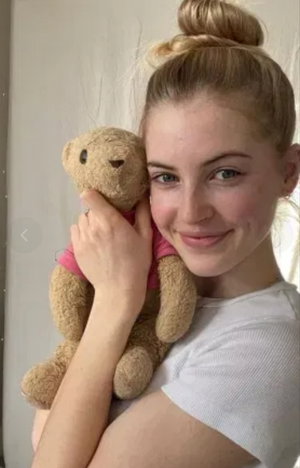 Blonde woman in white t-shirt holding teddy bear indoors.