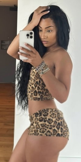 Woman with long black hair in leopard print top and shorts, taking mirror selfie indoors.
