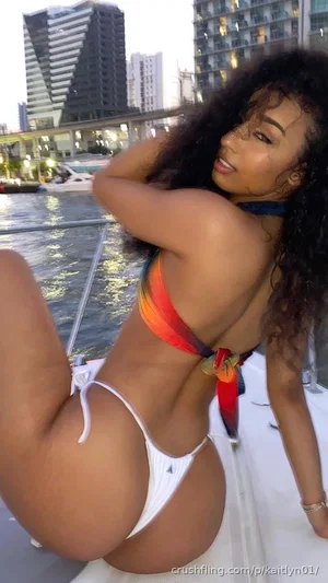 Woman in colorful bikini posing on boat with city skyline behind.