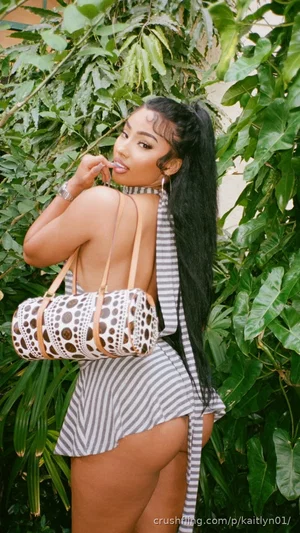 Woman in striped outfit posing outdoors near green foliage, holding patterned bag.