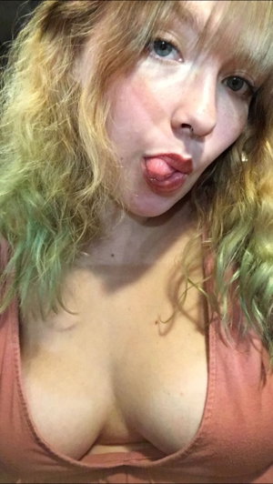Woman with colorful hair in pink top taking close-up selfie.