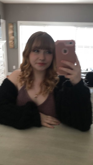 Blonde woman taking selfie in purple top and black sweater indoors.