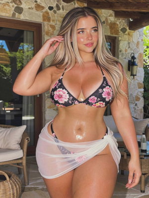 Woman in floral bikini top and sheer white wrap, standing on stone patio with outdoor furniture.