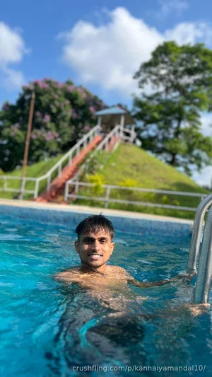 Man with short dark hair in a swimming pool, chest above water, outdoor setting with green hill and