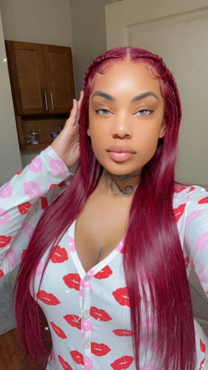Woman with long red hair and lip-print top, indoors, hand on head.