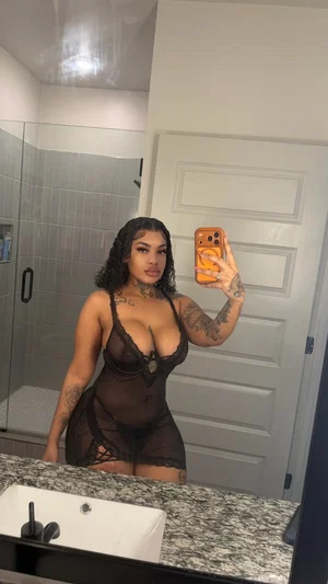 Woman in black lace bodysuit takes mirror selfie in bathroom.