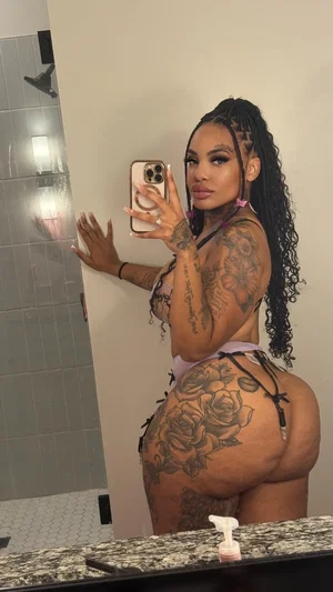 Woman with tattoos in lingerie taking mirror selfie in bathroom.