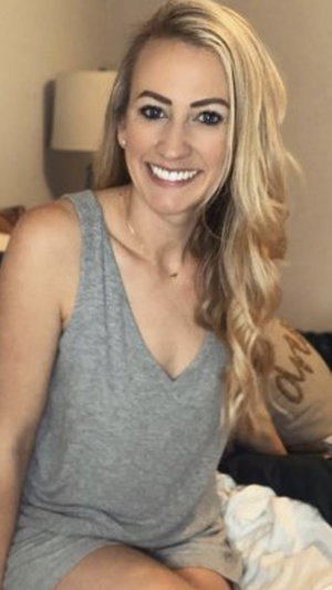 Blonde woman in gray tank dress on bed.