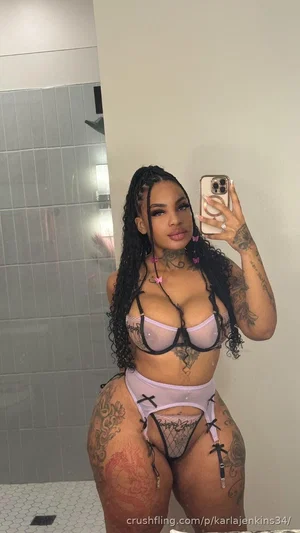 Woman with tattoos in lavender lingerie taking mirror selfie in bathroom.