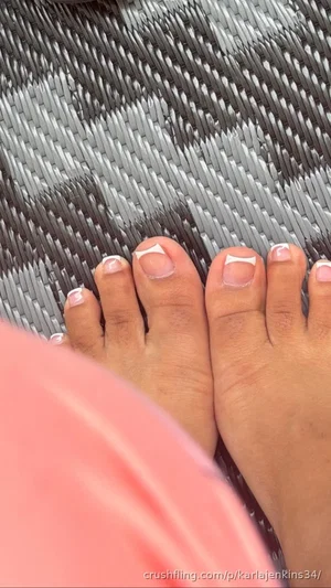 Close-up of feet with white nail polish on a woven gray surface, pink fabric visible.