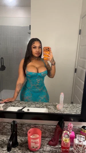 Woman in blue lace corset takes mirror selfie in bathroom, tattoos visible.