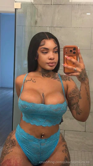 Woman with tattoos in blue lace lingerie taking mirror selfie in bathroom.
