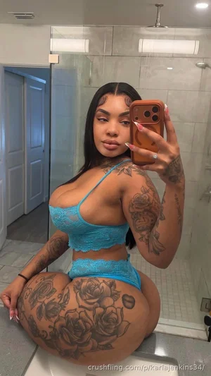 Woman in blue lace lingerie with tattoos, sitting on toilet in bathroom mirror selfie.