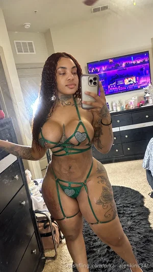 Woman with tattoos in green lingerie poses in bedroom selfie.