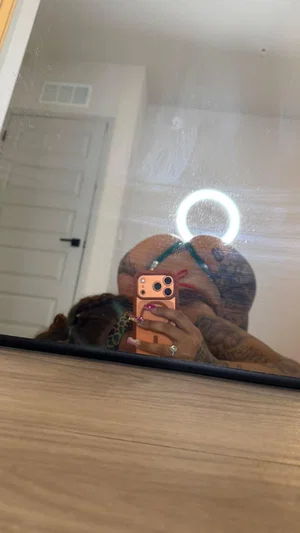 Woman with tattoos and colorful hair takes mirror selfie in indoor setting.