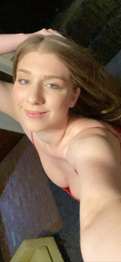 Woman with light brown hair in red top taking indoor selfie.