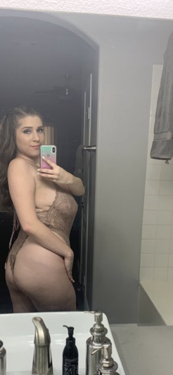 Woman in sheer lace lingerie taking mirror selfie in bathroom.