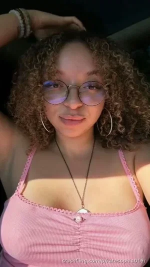 Woman with curly hair wearing pink top and glasses, indoors.
