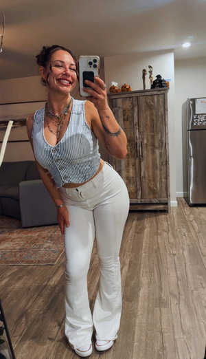 Woman in striped top and white pants takes indoor mirror selfie.