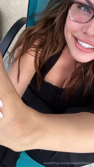 Woman with glasses and brown hair in black top, smiling in outdoor setting.