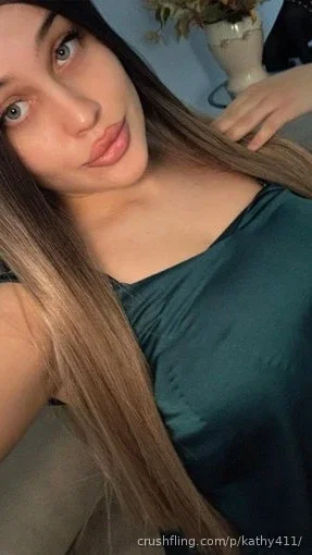 Woman with long brown hair in a teal top, taking a close-up selfie indoors.