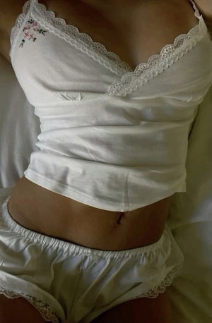 Woman in white lace-trimmed lingerie, showing midriff, lying on bed.