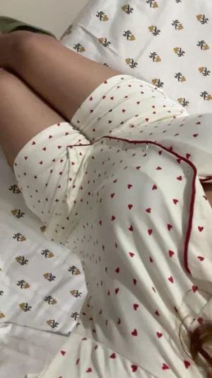 Person in white heart-patterned pajama shorts lying on patterned sheets.