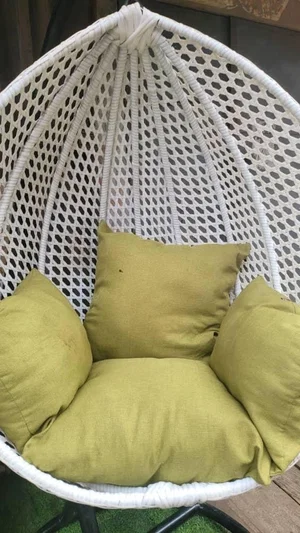 White wicker hanging chair with green cushions, outdoors on grass.