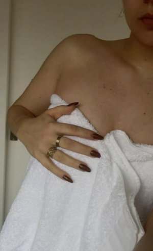 Woman holding white towel over bare chest indoors.