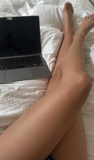 Woman's legs on white bed with laptop nearby.