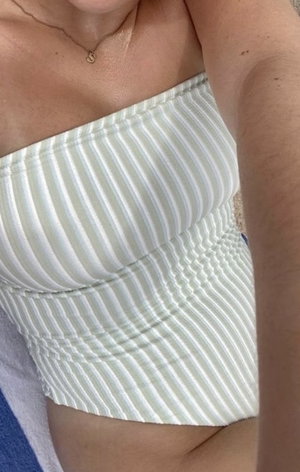 Woman in white striped strapless top, close-up of torso and arm, indoor setting.