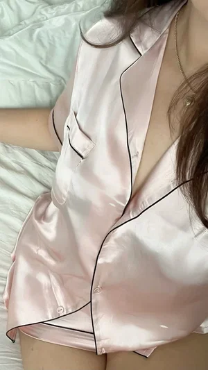 Woman in pink satin pajama top lying on bed, showing upper body and thighs.