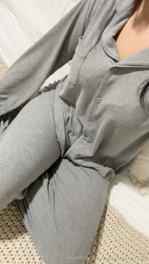 Woman in gray button-up loungewear sitting on bed, indoor setting.